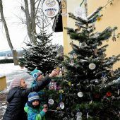 Kinder schmücken Christbäume mit ihren Basteleien