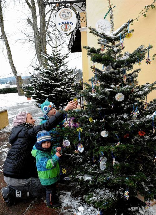 Kinder schmücken Christbäume mit ihren Basteleien