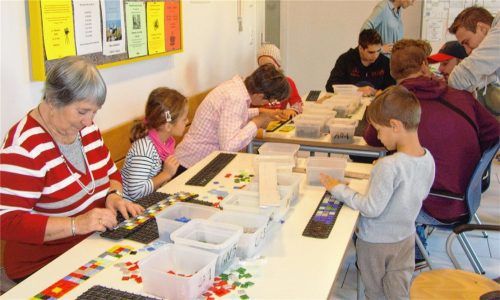 Senioren, Kinder und Jugendliche legen miteinander die Mosaikbänder, die in Tische und Bänke eingelassen werden.