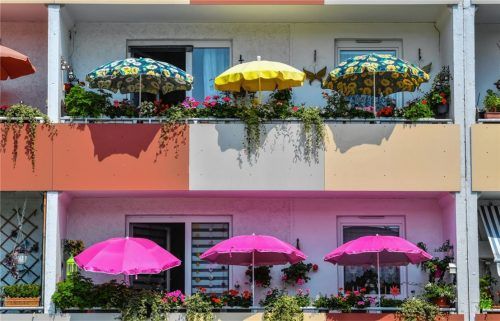 Sonnenschirme leuchten auf den Balkons eines Mehrfamilienhauses. Die Mietpreisbremse wurde zum Schutz der Mieter vor zu hohen Steigerungen erdacht. Kritiker werfen der Politik vor, damit nicht das Grundproblem für hohe Mieten – den Mangel an bezahlbarem Wohnraum – zu beheben. Foto dpa, Umfrage und Fotos: Hertl