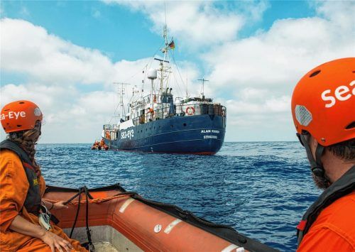 Zwei Seenotretter in einem Schlauchboot, die zum Rettungsschiff „Alan Kurdi“ hinüberschauen. Foto dpa