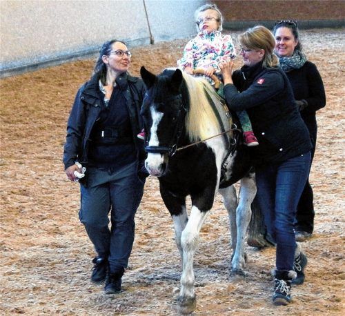 Die Bewegungen von Therapiepferd Acambaro werden auf die Muskulatur der kleinen Patientin Katharina übertragen, als würde sie selbst laufen. Immer dabei sind Therapeutin Jeannine Wagner (rechts) und eine Pferdeführerin, wie hier Bernadette Liebermann. Die Mutter des Kindes ist hier mit dabei (links). Foto Dinger