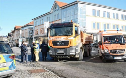 Polizeibeamte begutachten das Unfallfahrzeug, den orangefarbenen Kipplaster. Foto Ammelburger