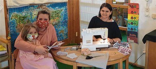 Im Kindergarten St. Johannes sitzt Marina Moser bei Kindergartenleiterin Corinna Ruff auf dem Schoß und hilft fleißig beim Zuschneiden der Stoffe. Annethres Purainer näht inzwischen die nächsten Masken.Foto re