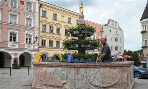 Kraiburgs historischer Brunnen ist wieder für den Sommer bereit: Ein Mitarbeiter des Bauhofs schrubbte Algen von Wänden und Boden. Auch die Blumen sind schon angebracht. Foto meling