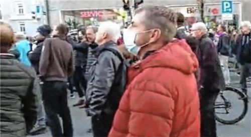 Ein Videoausschnitt: AfD-Politiker Andreas Kohlberger steht – in roter Jacke und mit Mundschutz – zwischen den Demonstranten. Foto Screenshot Facebook