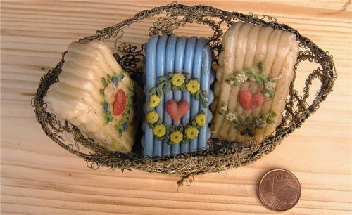 Drei „herzige“ Mini-Wachsstöcke im Drahtkörbchen (Münze zum Größenvergleich).