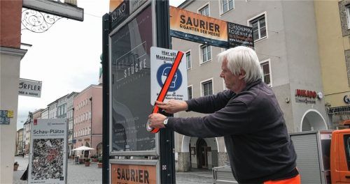Peter Huber vom Rosenheimer Bauhof klebt mit speziellem Abdeckband ein Schild in der Fußgängerzone ab, das die Maskenpflicht ausweist. Foto Schöne
