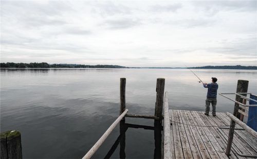 Ein Mann steht auf einem Steg bei Felden am Chiemsee und angelt. Zwei Männer mussten sich jetzt in Traunstein vor Gericht verantworten, weil sie am Chiemsee auf Rapfen-Jagd gegangen waren. Foto dpa
