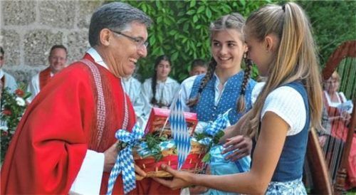 Die zwei Siegsdorferinnen Marina (rechts) und Clara überreichen Carlos Trovarelli einen Korb mit „Chiemgauer Erinnerungen“.