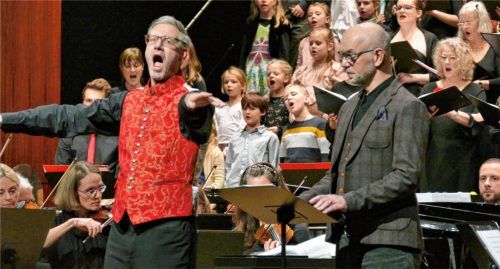Hochengagiert dirigiert Andreas Penninger neben seinem Chor und Kinderchor auch das Publikum, während Michael Althauser auf seinen nächsten Sprecherpart wartet. Foto janka