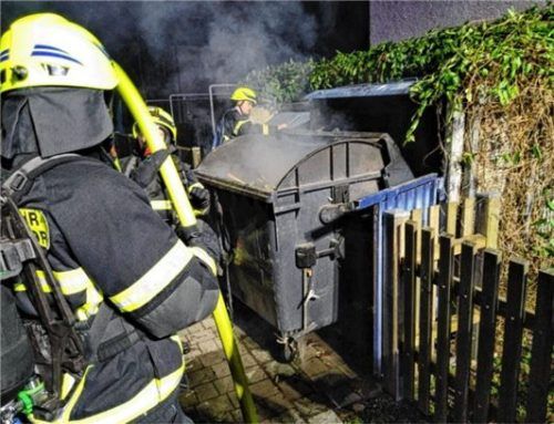Feuerwehrleute löschen eine Mülltonne.