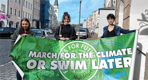 „Fürs Klima marschieren oder später schwimmen“ steht auf dem Plakat, das (von links) Nina Kozel, Fanny Weishäupl und Elisa Blatz von „Fridays for Future“ am Mühldorfer Stadtplatz ausrollen. Foto Latta