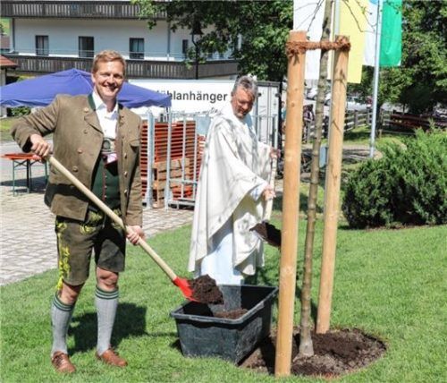 Bürgermeister Simon Frank (links) und Pfarrer Paul Janßen setzen einen Apfelbaum vor dem Pfarrheim.