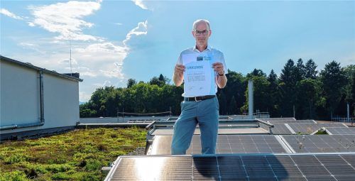 Der Technische Betriebsleiter Thomas Günther steht auf einem der begrünten Dächer eines Produktionsgebäudes und freut sich über die Urkunde zur zehnjährigen Mitgliedschaft.Foto re