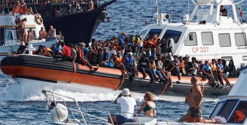 Ein Boot der italienischen Küstenwache transportiert Migranten unter der Beobachtung einer Gruppe von Touristen. Die Ankunft Tausender Bootsmigranten in kurzer Zeit hat die Insel Lampedusa an ihre Grenzen gebracht. Foto dpa