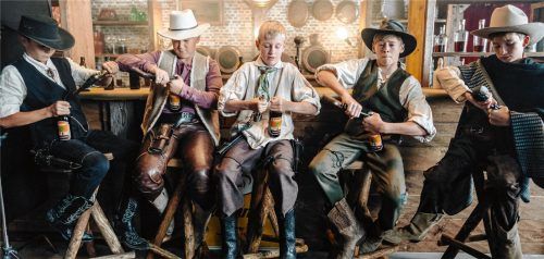 Die Spezi-Suchtis (von links) Flori, Korbi, Louis, Finn und Johannes versuchen in einer Drehpause an der Bar des Saloons, Spezi-Flaschen mit Pistolen zu öffnen. Foto Flötzinger Privatbrauerei Franz Steegmüller