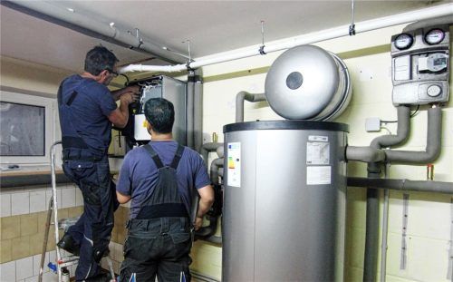 Zwei Handwerker installieren eine Wärmepumpe im Keller eines Hauses. Die Chefs der SHK-Innungen in der Region stehen hinter der Technik, doch sind sich aufgrund der politischen Rahmenbedingungen und der steigenden Stromkosten nicht mehr sicher, ob sie sie Kunden „reinen Gewissens“ noch empfehlen können. Foto dpa