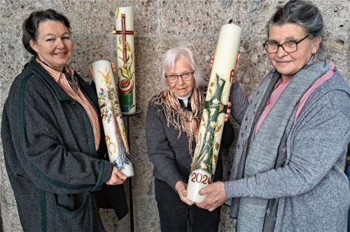 Rosa Rottmüller (rechts) zeigt die Kerze, die heuer in der Osternacht geweiht wird, Bärbel Merk (links) zwei Motive aus den Vorjahren. Mathilde Bayerlein hat die Girlanden gebunden, die die Kerzen und den Kerzenständer ummanteln.Foto Hadersbeck