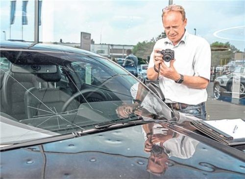 Dokumentation: Ein Sachverständiger untersucht den an Scheibe und Motorhaube sichtbaren Hagelschaden. Foto imago
