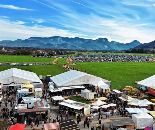 Blick vom Riesenrad: das Marktgelände und die mit Autos der Besucher zugeparkten Wiesen vor der Bergkette.