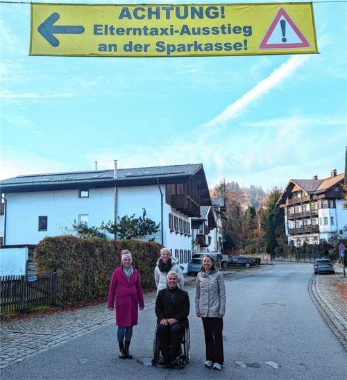 Mit diesem Straßenbanner, das quer über die Dorfstraße gespannt ist, wollen Schule, Elternbeirat und Gemeinde auf den anzusteuernden Bring- und Abholparkplatz an der Sparkasse aufmerksam machen. Ramona Astner (von links) und Veronika König vom Schulelternbeirat, Bürgermeister Hajo Gruber und Schuldirektorin Antje Radetzky hoffen, dass viele Eltern das Banner befolgen. Foto Hoffmann