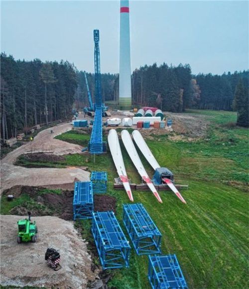 Vor dem finalen Aufbau lag der auffällig blaue Kran in Einzelteilen neben dem Windrad-Fundament. Die Flügel veranschaulichen die Größenverhältnisse. Jeder hat eine Länge von fast 80 Metern. Foto Schmuck