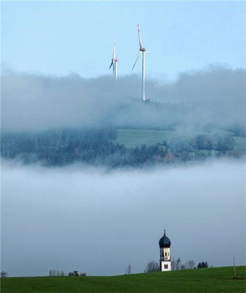 Windräder ragen hinter einem Kirchturm aus dem Nebel. Foto dpa