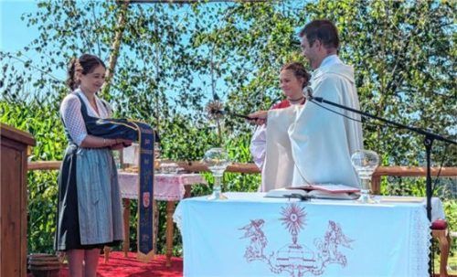 Die Erinnerungsfahne hielt Lisa Gropp (links) bei der Weihe durch Pfarrer Martin Ringhof (rechts) beim Gottesdienst auf dem ehemaligen Sportplatz in Schönbrunn.