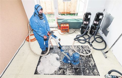 Ein Fachmann entfernt PVC-Fliesen sowie Kleber: Auch in Böden kann Asbest stecken. Foto Markus Scholz/dpa