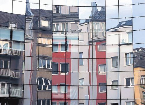 Häuser spiegeln sich in einer Fassade in der Kölner Innenstadt. Der Immobilienmarkt ist immer mehr internationale Strömungen unterworfen. Foto IMAGO/Panama Pictures