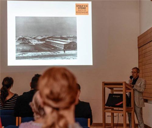 Dr. Thomas Nowotny von der Initiative Erinnerungskultur berichtete auf der Gedenkveranstaltung über das Schicksal der kleinen Rosa Reinhardt. Das projizierte Bild von den Baracken in Auschwitz bringt die Düsterkeit und die Hoffnungslosigkeit zum Ausdruck, mit der sich Sinti und Roma damals konfrontiert sahen.