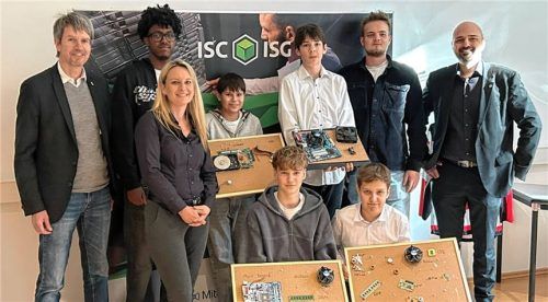 Gruppenbild mit den Schülern und ihren Komponentenboards: (von links, stehend) Andreas Bensegger, Azubi Nathan Kume, Personalleiterin Nadine Demmel, die Schüler Anaid und Jan, Azubi Leon Neidiger und Technischer Geschäftsführer Philip Crüwell sowie (von links, kniend) die Schüler Vincent und Andreas.Foto ISG Informatik Service