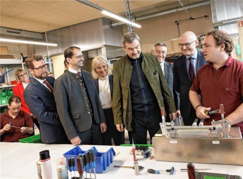 „Arbeit ist Teilhabe am Leben“: Ministerpräsident Markus Söder (Vierter von rechts) und Sozialministerin Ulrike Scharf (Dritte von links) ließen sich beim Besuch der Wendelstein- Werkstätten für Menschen mit Behinderung der Caritas in Rosenheim von einem Mitarbeiter die Aufgaben in der „Technischen Montage“ erklären. Foto StMAS/Nötel