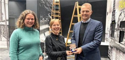 Goldener Gewinn zwischen Bauarbeiten: Lokschuppen-Leiterin Dr. Jennifer Morscheiser und Karl Göpfert, Vorstandsvorsitzender der Sparkasse Rosenheim-Bad Aibling, übergeben die Goldmünze an Gewinnerin Fiona Maierhofer. Foto Veranstaltungs- und Kongress GmbH