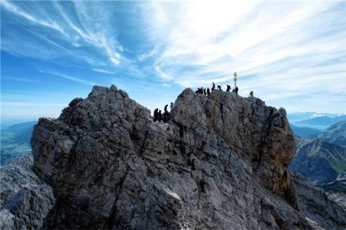 Ausflügler genießen das schöne Wetter am Gipfelkreuz auf der Zugspitze. Foto dpa