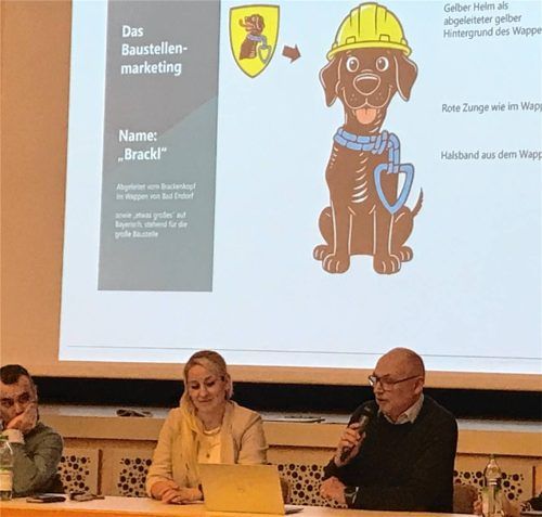 Der Baustellen-„Brackl“ wird die Bad Endorfer längere Zeit begleiten. Er wacht über die Informationen und weist auf Änderungen, bildlich gesprochen, auffallend hin. Tiefbaumaßnahmen in der Rosenheimer Straße, der geplante Hochwasserschutz und die Verkehrsführung über einen geplanten Kreisel in der Ortsmitte sind längerfristige Belastungen für den Ort. In der jüngsten Gemeinderatssitzung stellten (von links) Bürgermeister Alois Loferer und die beiden Quartiersmanager der CIMA Beratungs- und Management GmbH, Solveig Lüthje und Markus Jocher, unter anderem das Baustellen-Management vor.Foto Dachs