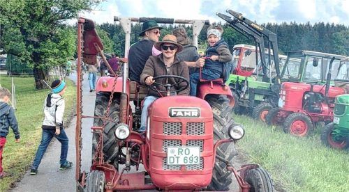 Beim Bulldogtreffen in Prien-Arbing fahren Erwachsene und Kinder auf einem roten Oldtimer-Traktor über das Veranstaltungsgelände, während viele Traktoren zur Besichtigung am Straßenrand aufgereiht sind. Foto Archiv Hötzelsperger