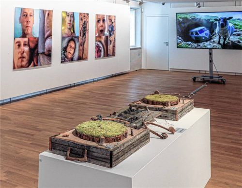 Blick auf das aus Naturmaterialien gestaltete DJ-Pult des Wiener Künstlers Uwe Bressnik aus dem Jahr 2000 im Vordergrund. An den Wänden zu sehen sind drei Fotografien aus der Serie „me and some friends“ von Uli Reiter (2016, Digitaldruck auf Alu Dibond, 130 x 130 cm) sowie ein Ausschnitt aus Reiters KI-Film „Narration kaputt“ von 2026.Foto  Effner