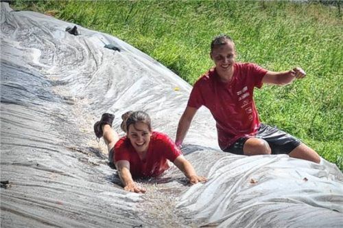 Teilnehmer rutschen auf einer nassen Schlammbahn einen Hang hinunter und haben sichtlich Spaß beim Hindernislauf „SchoniGaudiBazLauf“ in Schonstett. Foto Rieger