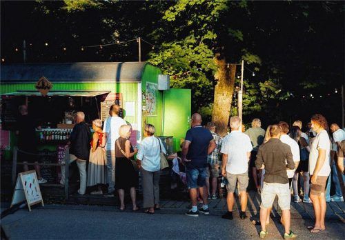 Besucher stehen im Abendlicht vor dem grünen Kiosk „Bramburi“ im Kulturbiergarten Schlange.