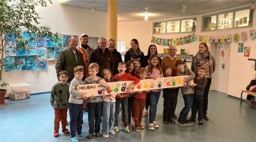 Kinder halten das beim traditionellen Firstklau gestohlene Brett, das heute mit ihren Handabdrücken verziert im Speisesaal des neuen Kinderhorts hängt.