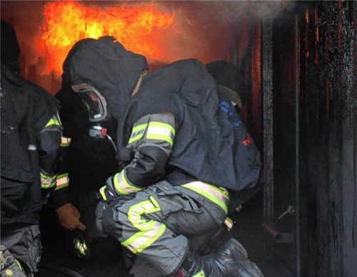 Feuerwehrleute trainieren im Brandübungscontainer, wo die Hitze nur am Boden erträglich ist. Die schwarzen Umhänge schonen Einsatzkleidung und Geräte. Foto Martin Binder