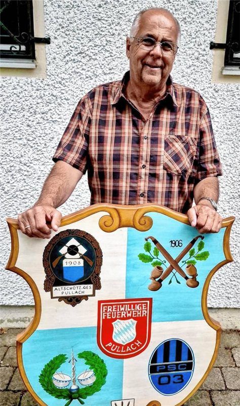 Hermann Tutschka, Vorsitzender des Pullacher Ortskartells, mit einem Schild, auf dem die Wappen beziehungsweise Logos der fünf Pullacher Vereine abgebildet sind. Foto re