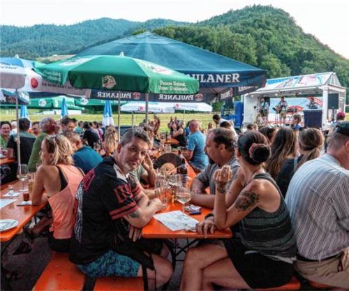 Zahlreiche Gäste genossen das Dorffest der Unterwössner Feuerwehr an Tischen unter Sonnenschirmen, während im Hintergrund eine Band spielt. Foto Ludwig Flug