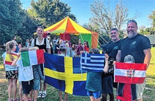 Kinder posieren mit Flaggen der jeweiligen Länder, zusammen mit der Betreuerin Sarah Borrmann (von links), Markus Bundel, der für das Ferienprogramm federführend zuständig ist, und dem Geschäftsführer des Stadtjugendrings, Florian Robida (von rechts). Foto Christine Leuthe