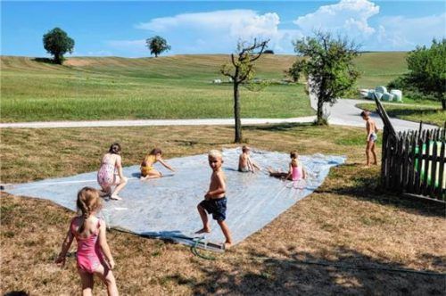 Kinder vergnügen sich auf einer Wasserrutsche aus Silofolie auf einer Wiese. Foto  Rieder