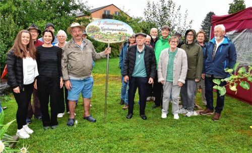 Raimund Ratzka und Johann Hamberger (links und rechts neben dem Schild) enthüllen das Namensschild „Johann Hambergers Gartenparadies“ in Stephanskirchen, umgeben von Gärtnern, die trotz Regenwetters zum Festakt und Gartenfest gekommen sind. Foto Schlecker