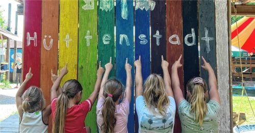 Teilnehmende Kinder zeigen auf das in Regenbogenfarben bemalte Schild mit der Aufschrift „Hüttenstadt“. Foto Stadtjugendring Rosenheim