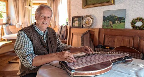 Der bayerische Musiker und Zithersolist Hans Berger spielt lächelnd auf einer Zither in einer gemütlichen, holzgetäfelten Stube.Rainer Nitzsche